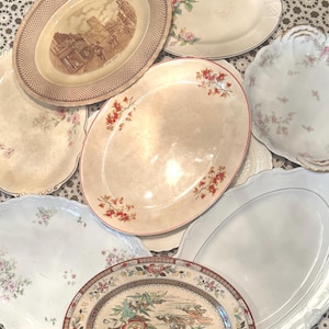 Könnte beinhalten: Eine Sammlung von acht ovalen Keramikplatten und Tellern mit verschiedenen Designs, darunter braune architektonische Szenen, zarte rosa und rote Blumenmuster sowie komplizierte mehrfarbige botanische Motive mit gewelltem Rand.