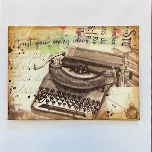 May include: A rectangular artwork featuring a vintage typewriter illustration with the text "Trust your crazy ideas." The artwork has a distressed, aged appearance with sepia tones, splatters, and script-like elements.