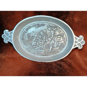 May include: Oval pewter serving tray with handles. The tray features a raised relief scene of people ice skating with the words "REJOICE AND BE GLAD" around the edge. The tray is silver in color.