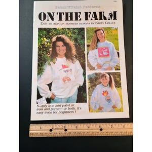 Puede incluir: Una portada de revista titulada "ON THE FARM" con el texto "Easy to Iron On Transfer Designs by Barry Geller". La portada presenta tres fotos de personas que usan sudaderas blancas con diseños de animales de granja. Una regla está en la parte inferior.