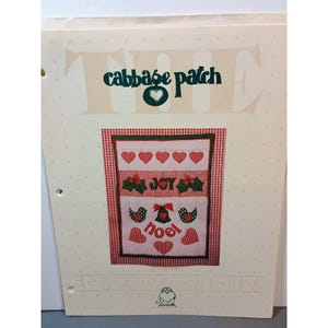 Può includere: Una pagina di "The Cabbage Patch" designer cut-ups. La pagina presenta un motivo a quadri rossi e bianchi con un design patchwork. Il patchwork include cuori, agrifoglio, uccelli, campane e le parole "JOY" e "noel". Il titolo "The Cabbage Patch" è in alto.