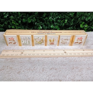 May include: A white ceramic mug with a black handle and the text "But First, Coffee" in a black, bold font. The mug is on a white surface.