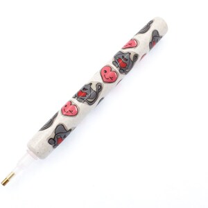 May include: A white pen with a clear tip and a gold metal point. The pen is decorated with a repeating pattern of pink hearts and gray cats.