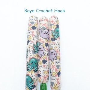 May include: Three Boye crochet hooks with a sea-themed design. The hooks are white with a pattern of blue and pink sea creatures, including octopuses and seals.