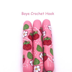 Pode incluir: Três agulhas de crochê cor-de-rosa com um padrão de morangos e flores. As agulhas são etiquetadas como "Boye Crochet Hook".