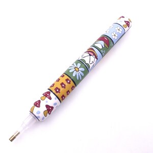 Könnte beinhalten: Ein bunter Stift mit weißem Hintergrund und einem Muster aus Pilzen, Blumen und einem Regenbogen. Der Stift hat eine durchsichtige Kunststoffspitze.
