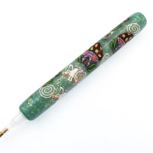 Könnte beinhalten: Ein grüner Glitzerstift mit weißer Spitze und einem goldenen Metallende. Der Stift ist mit bunten Pilz- und Feenmotiven verziert. Der Stift ist für das Diamond Painting bestimmt, ein Handwerk, bei dem winzige Harzdiamanten auf eine Leinwand aufgetragen werden.