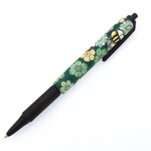 Könnte beinhalten: Ein schwarzer und grüner Stift mit einem floralen Design mit Bienen und Blumen. Der Stift hat eine schwarze Kappe und eine goldene Spitze.