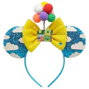 May include: Blue headband with a yellow bow and a house with balloons on top. The ears are blue with white clouds.