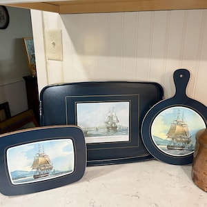 May include: Three blue and gold trays with images of sailing ships. The trays are on a white countertop.