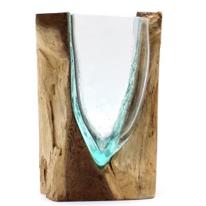 May include: A clear glass vessel with a light blue tint, shaped to fit into a vertical, rough-hewn piece of natural brown wood. The glass has a smooth, curved surface and is securely nestled within the textured, organic grain of the wood base.