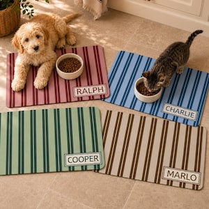 Peut inclure: Quatre tapis de nourriture rectangulaires pour animaux avec des rayures verticales bordeaux, bleues, vertes et marron. Chaque tapis comporte une étiquette blanche avec les noms RALPH, CHARLIE, COOPER et MARLO en noir. Deux bols blancs.