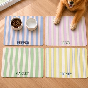 Peut inclure: Quatre tapis de repas rectangulaires pour animaux avec des rayures verticales bleues, violettes, vertes et jaunes. Chaque tapis porte un nom personnalisé imprimé au centre : PEPPER, LUCY, MARLEY et HONEY. Deux bols blancs sont posés dessus.