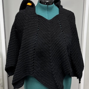 May include: Black crochet hooded poncho with a yellow flower detail. The poncho is draped over a mannequin.