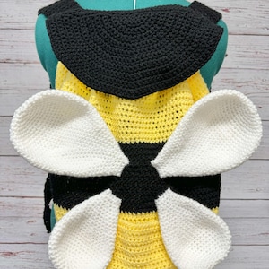 May include: A handmade crochet bee costume, featuring a black and yellow striped body, a black collar, and large white wings. The costume is displayed on a mannequin, showcasing the details of the crochet work.