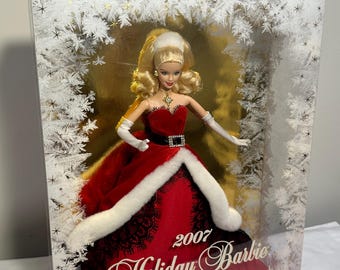 Puede incluir: Muñeca Barbie Holiday de 2007 en una caja decorativa. La muñeca viste un vestido rojo con ribete de piel sintética blanca y detalles de encaje negro. La caja presenta un fondo dorado con diseños de copos de nieve blancos y el texto "Holiday Barbie".