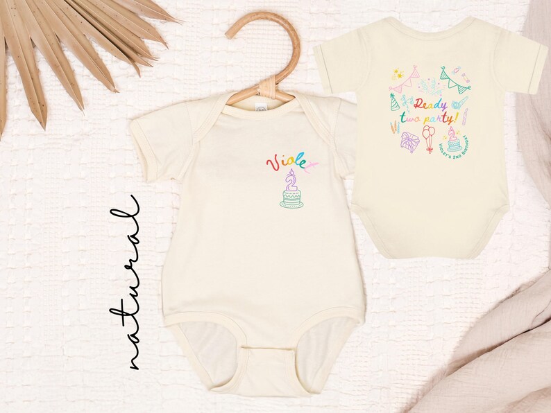 May include: Two natural-colored baby bodysuits. The left bodysuit features the name Violet and a birthday cake graphic. The right bodysuit displays the text Ready two party! surrounded by colorful illustrations of party hats, balloons, and gifts.