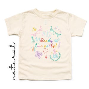 May include: A cream-colored short-sleeve t-shirt featuring a colorful graphic print with the text Ready two party! and Violet's 2nd Birthday. The design includes illustrations of party hats, bunting, balloons, a gift, and a birthday cake.