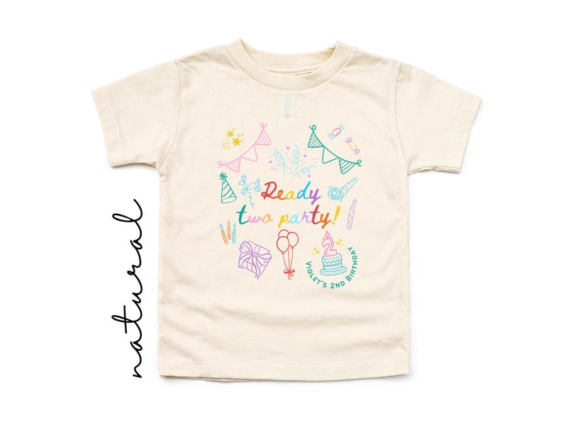 May include: A cream-colored short-sleeve t-shirt featuring a colorful graphic print with the text Ready two party! and Violet's 2nd Birthday. The design includes illustrations of party hats, bunting, balloons, a gift, and a birthday cake.