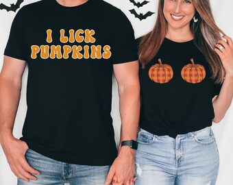 May include: Black t-shirts with Halloween-themed designs. One shirt has the text "I LICK PUMPKINS" in orange lettering. The other shirt features two orange and yellow plaid pumpkins. Both shirts are worn by a couple.
