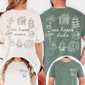 May include: Ivory and moss green t-shirts with camping-themed graphics. The ivory shirt says "one happy mama" and the moss green shirt says "one happy dada." Both shirts have a small graphic on the front and a larger design on the back.