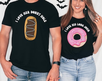 Op de afbeelding: Zwarte t-shirts met donutontwerpen. Eén shirt toont een chocolade-eclair met de tekst "I love her donut hole". De andere heeft een roze donut en zegt "I love his long john".
