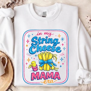 Könnte beinhalten: Weißes Sweatshirt mit farbenfroher Grafik. Die Grafik zeigt "in my String Cheese MAMA era" in blauen und rosa Buchstaben, mit einem Käsebündel und Sternen.