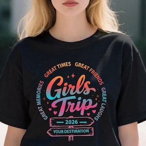 Może przedstawiać: Czarny t-shirt z kolorową grafiką z napisem "Girls Trip 2026". Projekt zawiera słowa "Great Times, Great Friends, Great Memories, Great Laughs" wokół centralnego tekstu. Poniżej dwa drogowskazy z napisem "Your Destination".