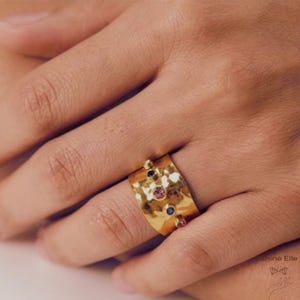 May include: Gold ring with a hammered texture and colourful gemstones. The ring is wide and has a rounded shape.