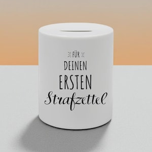 Könnte beinhalten: Ein weißer zylindrischer Sparschwein mit einem Schlitz oben. Der Text "FÜR DEINEN ERSTEN Strafzettel" ist in schwarzer Schrift auf der Vorderseite aufgedruckt. Der Hintergrund ist ein Farbverlauf aus Orange und Weiß.