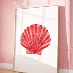 Puede incluir: Una impresión enmarcada con una ilustración de concha roja. La obra de arte está sobre un fondo blanco, con un marco dorado. La imagen se muestra sobre un suelo de madera clara, con una pared rosa de fondo.