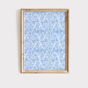 May include: A framed print with a blue and white abstract pattern of wavy lines. The print is in a light wood frame.