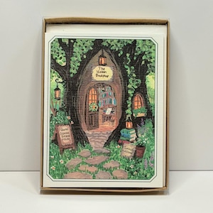 May include: A rectangular greeting card featuring a painting of a tree trunk shaped like a shop entrance with the text The Hidden Bookshop, Books Stories Dreams Inside, and Curious Welcome. The scene includes lanterns, books, and a stone path.