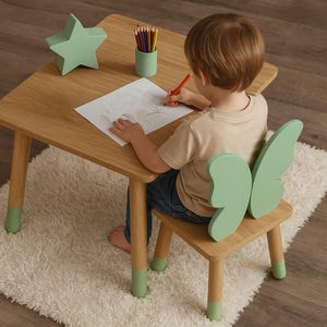 Peut inclure: Un enfant est assis à une table en bois avec une chaise en forme de papillon verte. La table a des pieds peints en vert et un veilleuse en forme d'étoile verte. L'enfant dessine sur une feuille de papier avec des crayons de couleur.