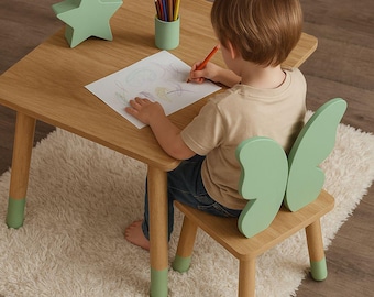 May include: A child sits at a wooden table with a green butterfly-shaped chair. The table has green painted legs and a green star-shaped nightlight. The child is drawing on a piece of paper with colored pencils.