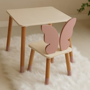 Può includere: Un set di tavolo e sedia in legno bianco con uno schienale a forma di farfalla sulla sedia. La sedia e il tavolo hanno accenti rosa.