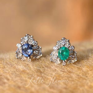 Könnte beinhalten: Ein Paar silberne Ohrringe mit einem floralen Design. Ein Ohrring hat einen blauen Edelstein, während der andere einen grünen Edelstein hat.