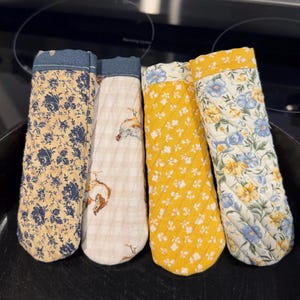 May include: Four quilted oven mitts with floral and farm animal patterns. The mitts feature a variety of colors, including yellow, blue, and cream. The mitts are designed to protect hands from heat while cooking.