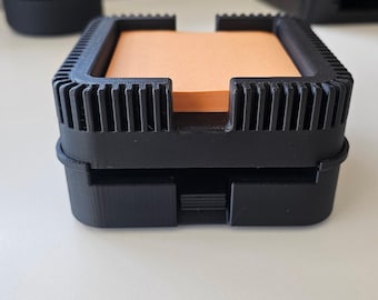 May include: A black plastic desk organizer with a built-in dispenser for sticky notes. The dispenser holds a stack of orange sticky notes.