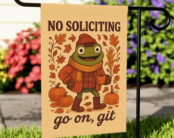 Könnte beinhalten: Eine beige Gartenflagge mit dem Text "NO SOLICITING" und "go on, git". Die Flagge zeigt einen Cartoon-Frosch mit Hut, Schal und Mantel, der eine Tasse hält, mit Kürbissen und Herbstblättern. Die Flagge wird auf einem schwarzen Metallständer im Garten gezeigt.