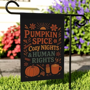 May include: Black garden flag with the text "Pumpkin Spice, Cozy Nights & Human Rights" in orange, green, and white. The flag features illustrations of a pumpkin, cinnamon sticks, and a mug of coffee. The flag is displayed on a black metal stand.