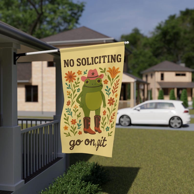 May include: A rectangular, cream-colored flag with the text "NO SOLICITING" at the top. The flag features a cartoon frog wearing a cowboy hat and boots, surrounded by floral designs. The words "go on, git" are at the bottom.