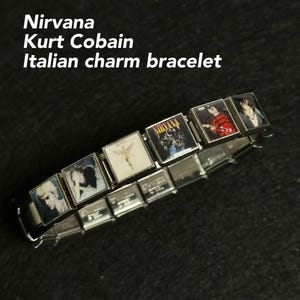 May include: Silver Italian charm bracelet featuring images of Nirvana and Kurt Cobain. The bracelet has multiple rectangular charms with various graphics, including album art and portraits. The text "Nirvana Kurt Cobain Italian charm bracelet" is visible.