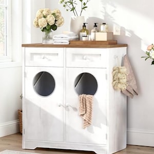 May include: A white cabinet with two doors and two drawers. The cabinet has circular openings and a wooden countertop. A towel hangs from the side. The cabinet is in a bathroom setting with flowers and toiletries.