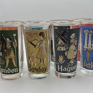 May include: Set of vintage drinking glasses with gold rims, featuring illustrations and city names like London, Bombay, The Hague, and Athens. Each glass has a different color background and design, showcasing iconic imagery.