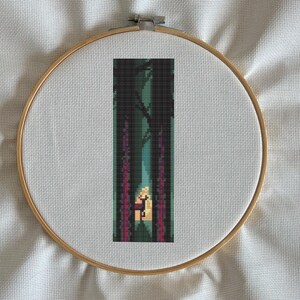 May include: Cross-stitch embroidery of a forest scene, framed in a wooden hoop. The design features a path through dark trees with a figure in the distance, rendered in shades of green, purple, and yellow.