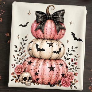 May include: A white fabric featuring a stack of three pumpkins. The top pumpkin is pink with a large black bow, the middle is cream with black bats and stars, and the bottom is pink with black stars. A skull and pink roses decorate the base.