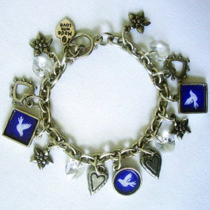 Puede incluir: Un brazalete de plata con una variedad de dijes, incluyendo corazones, flores, palomas y un dije que dice "Made with Love".
