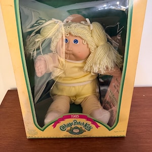 May include: A white ceramic mug with a black handle and the text "But First, Coffee" in a black, bold font. The mug is on a wooden surface. The mug is approximately 10 cm tall.