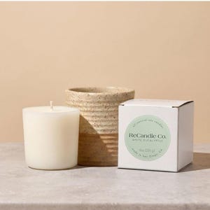 A white eucalyptus scented soy wax candle refill placed next to it’s box and a handmade, ceramic refillable candle jar